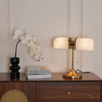 In this photo, a Clérachic gold table lamp with white ribbed shades lit on a walnut chest of drawers, beside a black glass vase and white orchids.
