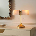 Pictured here, a Clérachic gold table lamp with pink-toned ribbed shades glowing, beside a gilt-leaf mirror on a cream console.