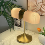 This Clérachic gold table lamp glows warm through its pink ribbed shades, with a fern, a book and an orange tulip behind.