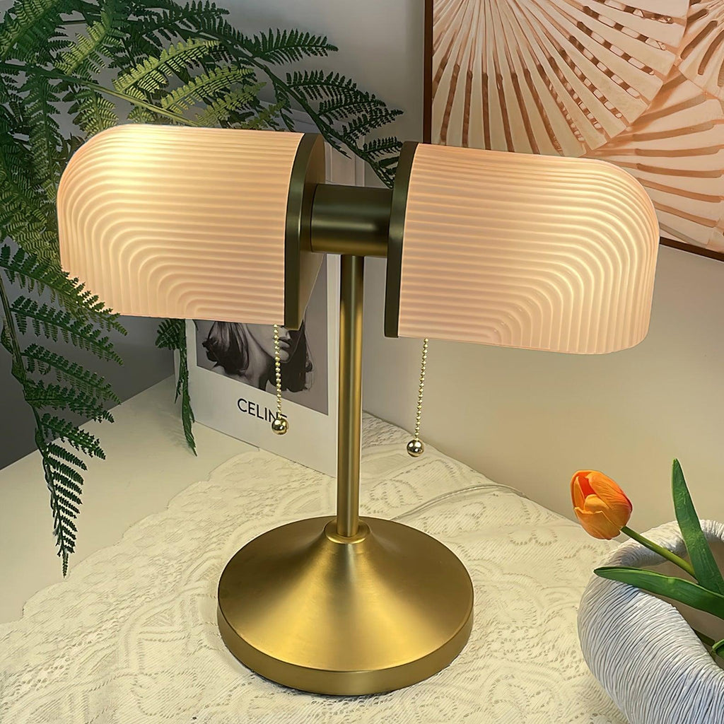 Warm light glows through the pink ribbed shades of this Clérachic gold table lamp, with a fern and a tulip around it.