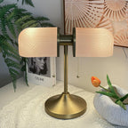 Close view of this Clérachic gold table lamp with pink ribbed shades, standing on a white lace cloth by a ceramic bowl.