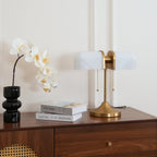 Shown here, a Clérachic gold table lamp with white ribbed shades sits at the right of a walnut chest, with a black glass vase and white orchids.