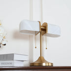 Angled close view of the white ribbed glass shades and brass stem of this Clérachic table lamp, with a stack of books beside it.