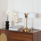 This Clérachic gold table lamp with white ribbed shades stands on a walnut chest with a rattan panel, below a spray of orchids.