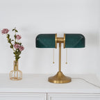 Pictured here, a Clérachic gold table lamp with dark green ribbed shades stands on a white cabinet, beside a wire vase of mauve roses.