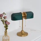 Angled view of this Clérachic gold table lamp with dark green shades and a flared satin gold base, beside a vase of roses.