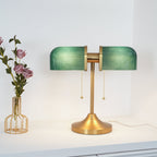 Warm light fills the green ribbed shades of this Clérachic gold table lamp, which stands next to a vase of dusky pink roses.
