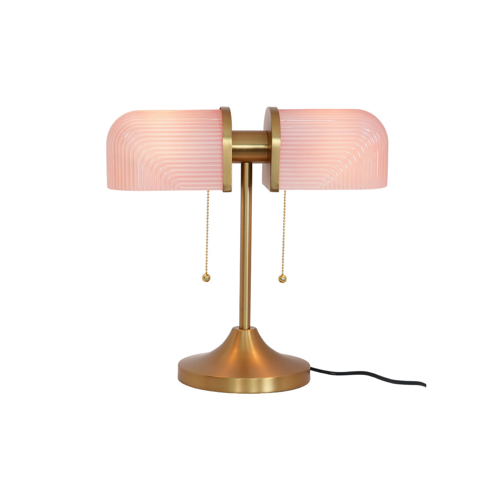 In this photo, a Clérachic gold table lamp with pink ribbed shades and its black cord, shown on a plain white backdrop.
