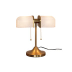 Pictured here, a Clérachic gold table lamp with warm white ribbed shades, lit, with a black cord trailing from its flared gold base.