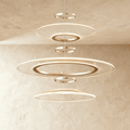 Clérachic three-tier gold ring chandelier with mesh acrylic discs and slim LED edges, hung against a limewashed wall.
