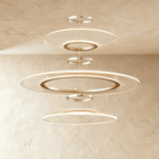Clérachic three-tier gold ring chandelier with mesh acrylic discs and slim LED edges, hung against a limewashed wall.