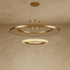 Clérachic two-ring gold LED chandelier with a large mesh-filled ring over a smaller lit acrylic disc, shown on plaster.
