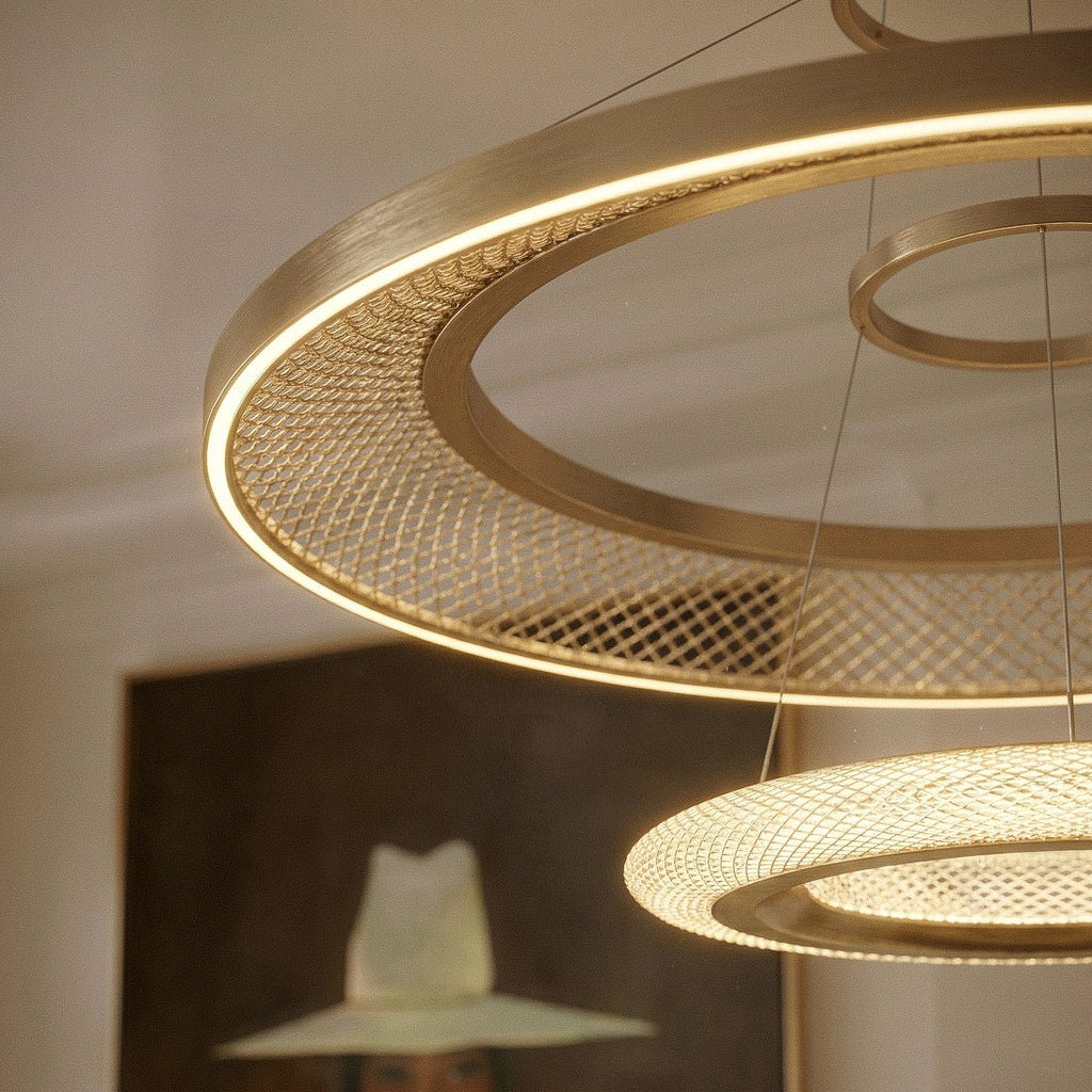 Close detail of a Clérachic brushed gold LED ring with a woven mesh acrylic panel and a smaller glowing disc below.