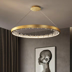 Gold Clérachic ring pendant light lit under a grey ceiling, with dark curtains and a black and white portrait print on the wall.