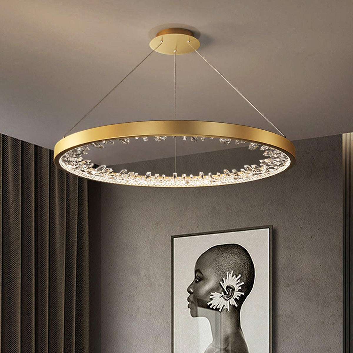 Gold Clérachic ring pendant light lit under a grey ceiling, with dark curtains and a black and white portrait print on the wall.
