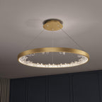 Gold Clérachic ring pendant light with a round ceiling plate and crossed cables, hanging in front of a dark panelled wall.
