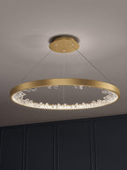 Gold Clérachic ring pendant light lit above a dark panelled wall, its three cables running up to a round gold ceiling plate.