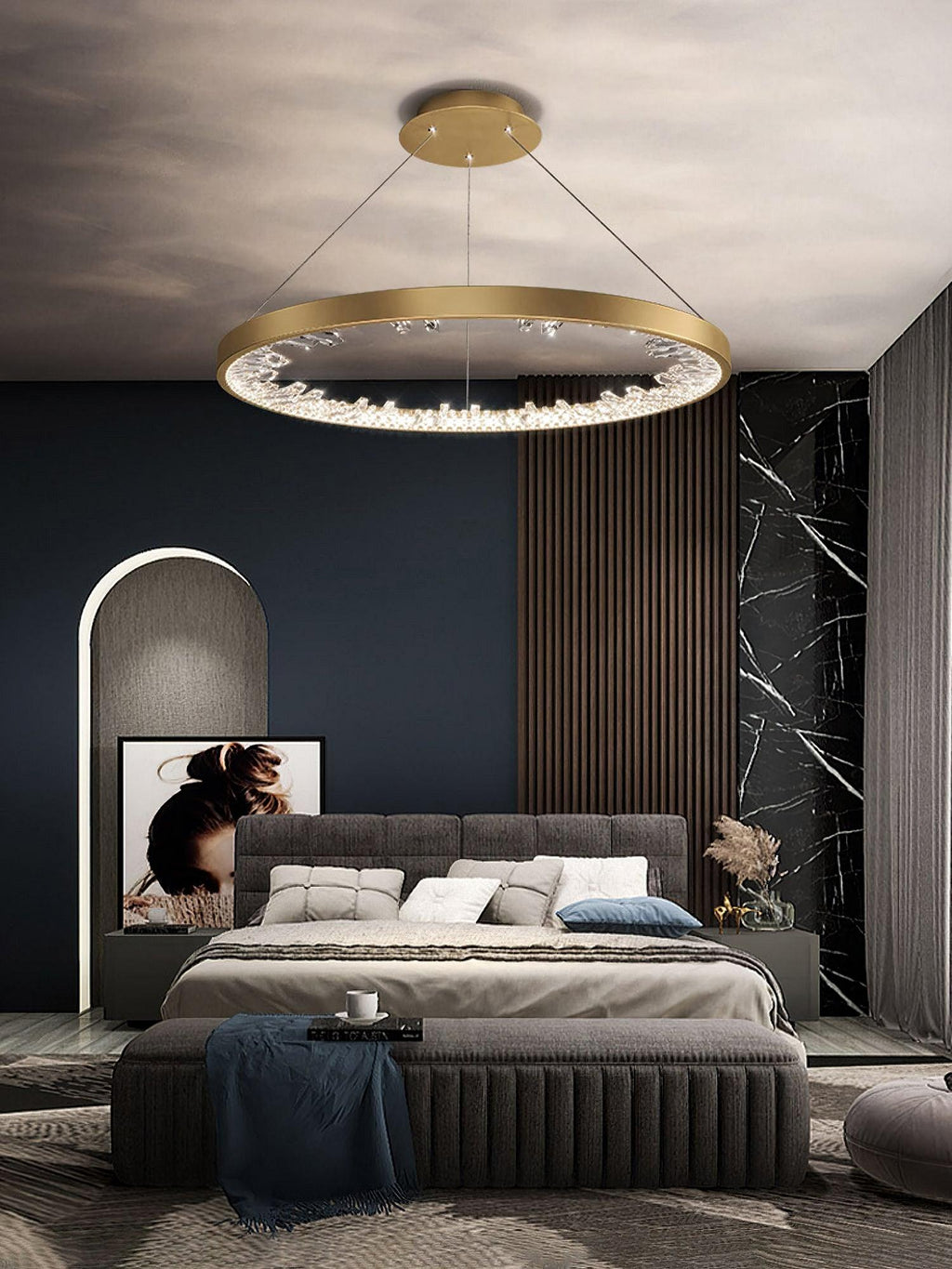 Gold Clérachic ring pendant light above a bedroom with a grey tufted bed, a marble feature wall and wood slat panelling.