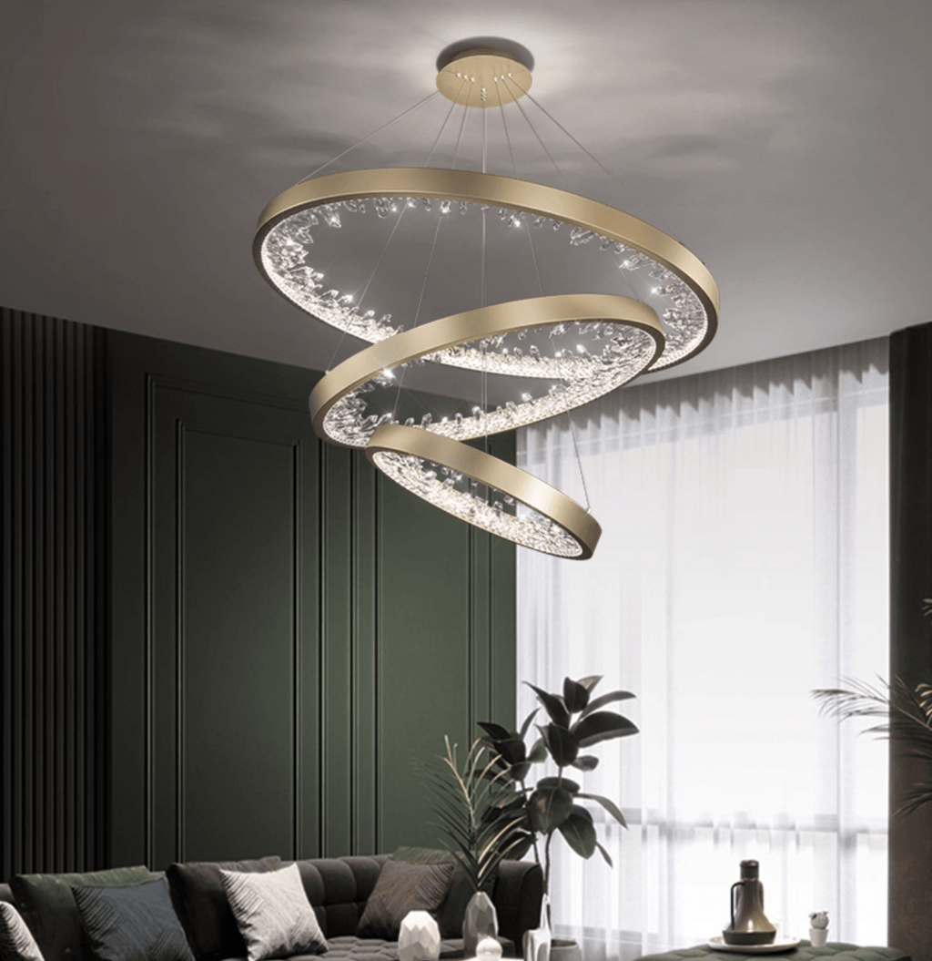 Three gold Clérachic ring pendants stacked at different angles in a dark green room, beside sheer curtains and a grey sofa.