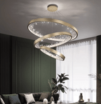 Three gold Clérachic ring pendants stacked at different angles in a dark green room, beside sheer curtains and a grey sofa.