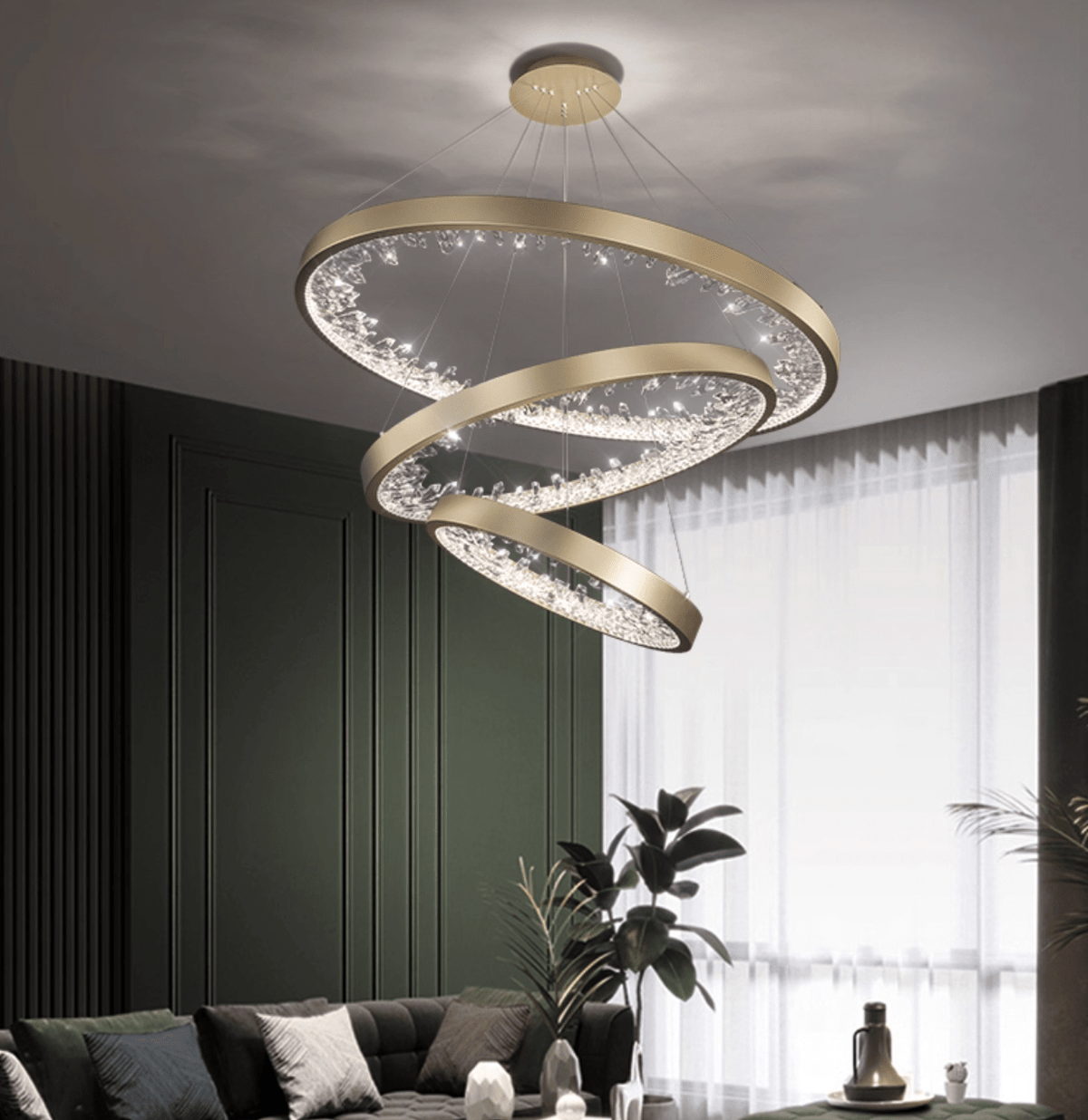 Three gold Clérachic ring pendants stacked at different angles in a dark green room, beside sheer curtains and a grey sofa.