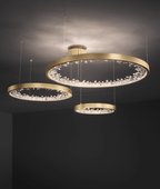 Three gold Clérachic ring pendants of different sizes lit at different heights in a dark room, their clear glass pieces sparkling.