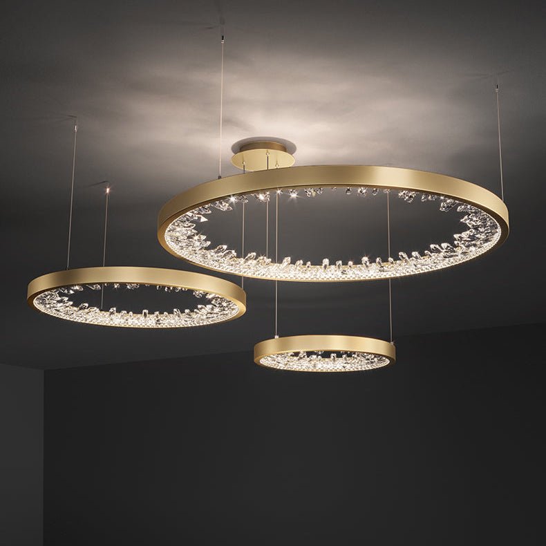 Three gold Clérachic ring pendants hung at different heights below a grey ceiling, the clear shades glowing along each band.