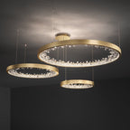 Three gold Clérachic ring pendants hung at different heights below a grey ceiling, the clear shades glowing along each band.