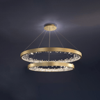 Two gold Clérachic ring pendants hung one above the other, lit against a dark blue-grey ceiling.