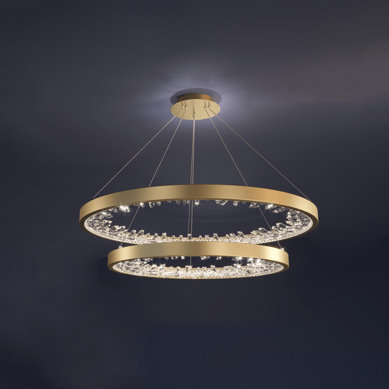 Two gold Clérachic ring pendants hung one above the other, lit against a dark blue-grey ceiling.