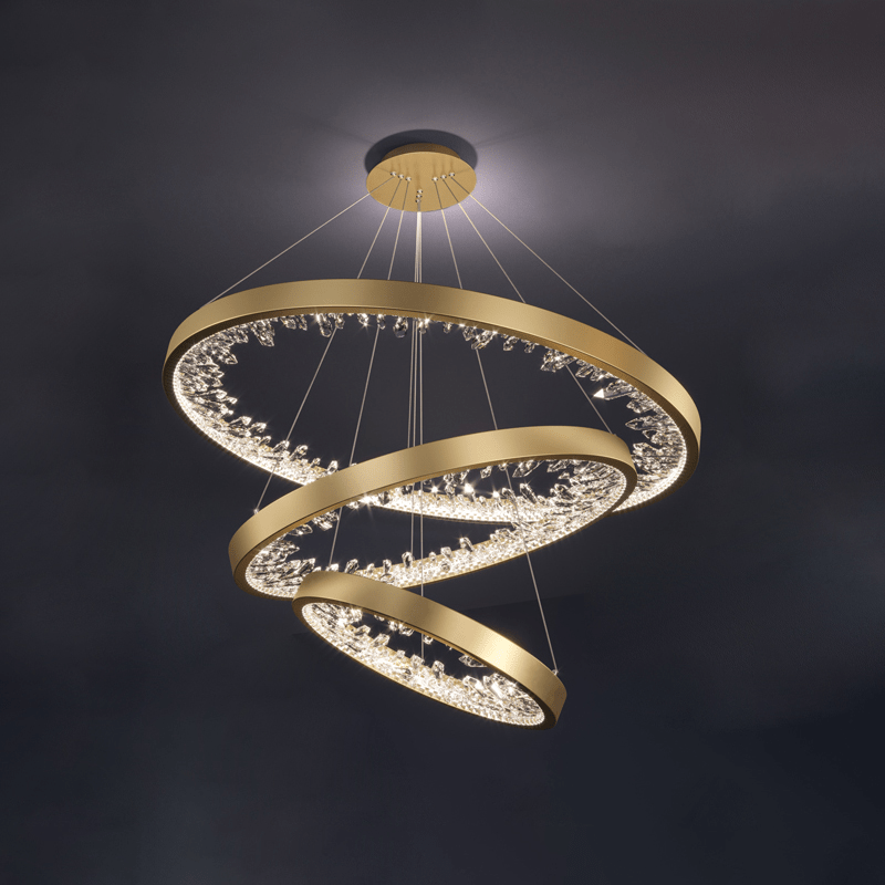 Three gold Clérachic rings stepped down from one ceiling plate, with clear glass pieces lit around each band against a dark backdrop.