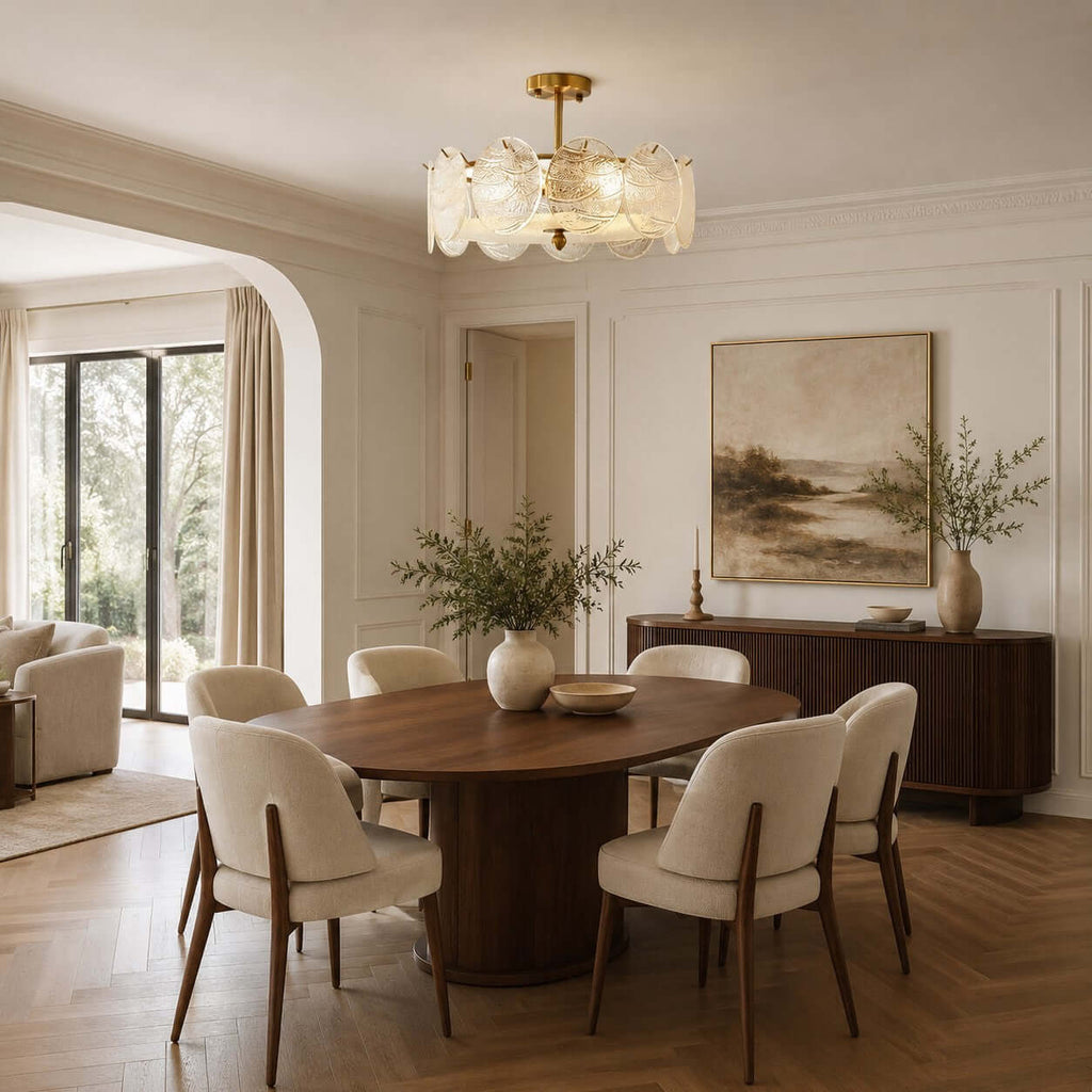 A Clérachic semi flush light with gold fittings hangs over an oval walnut dining table, cream chairs and a herringbone floor.