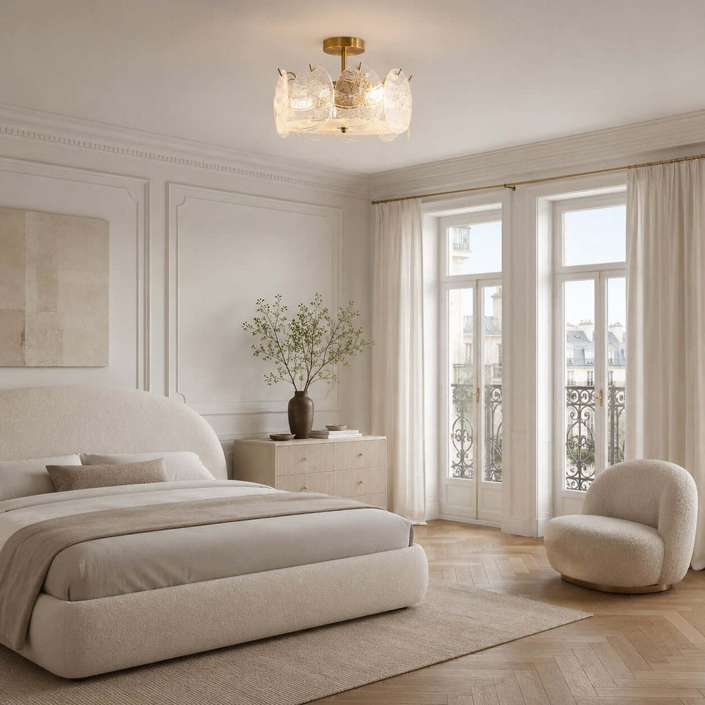 A Clérachic semi flush light sits above a rounded cream bed and a boucle armchair, near tall balcony doors and a herringbone floor.