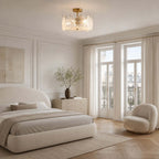A Clérachic semi flush light sits above a rounded cream bed and a boucle armchair, near tall balcony doors and a herringbone floor.