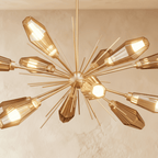 Close view of the Clérachic gold starburst chandelier, hexagonal amber glass heads lit warm between fine gold spikes.