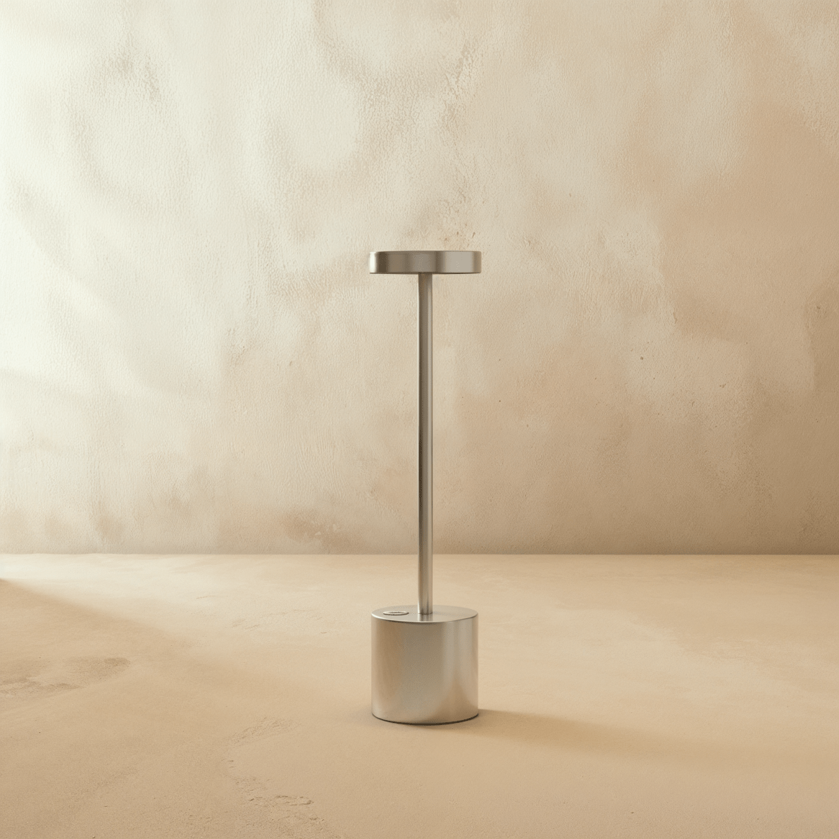 Clérachic cordless table lamp in brushed silver, disc shade on a slim stem above a cylindrical base against a plaster wall.