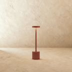 Clérachic cordless table lamp in a warm terracotta finish, disc shade glowing above a slim stem and round base.