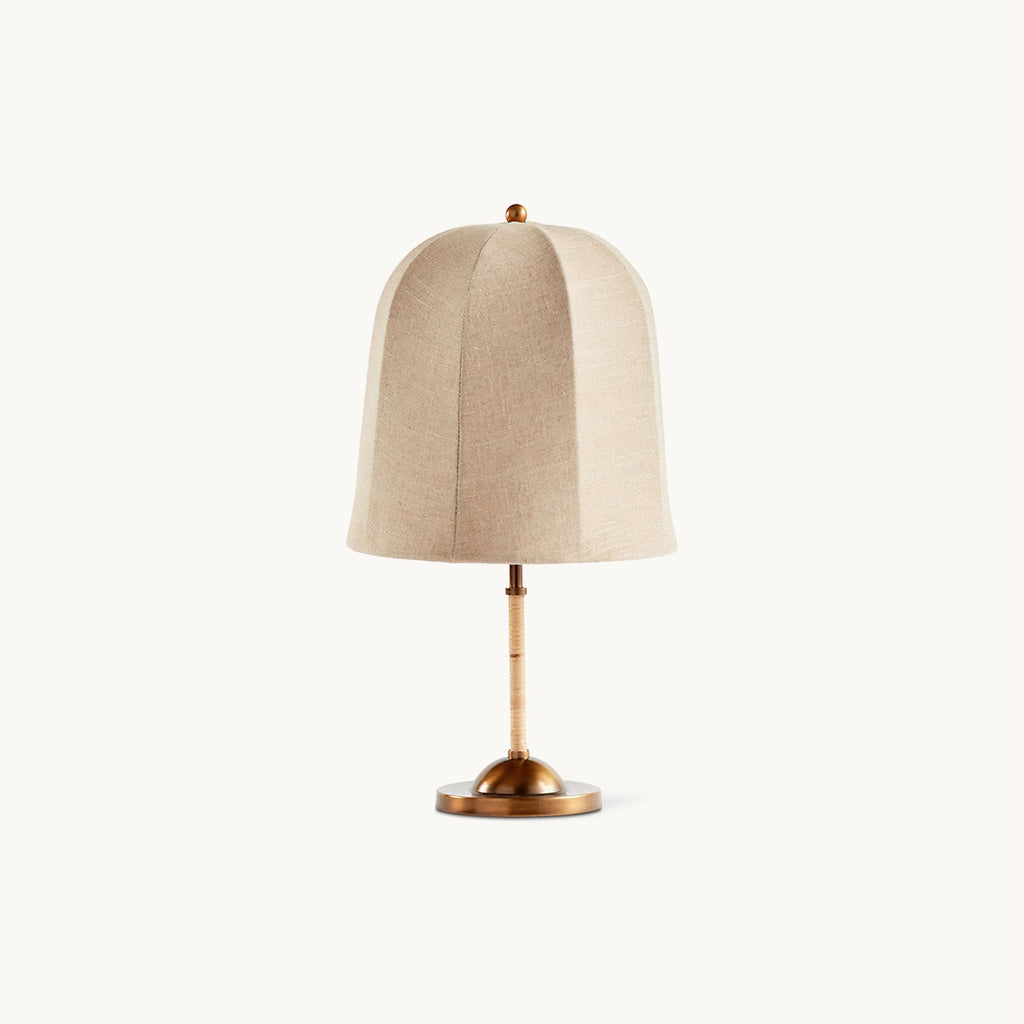 A Clérachic table lamp with a bell-shaped linen shade, a slim bamboo-wrapped stem and a gold base, on a plain white backdrop.
