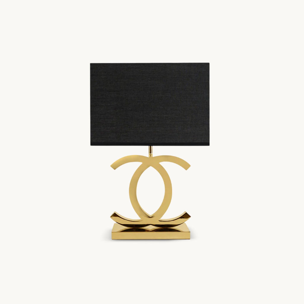 Clérachic gold table lamp with a black rectangular fabric shade on a polished stainless steel base of two interlocking curved loops, on white.