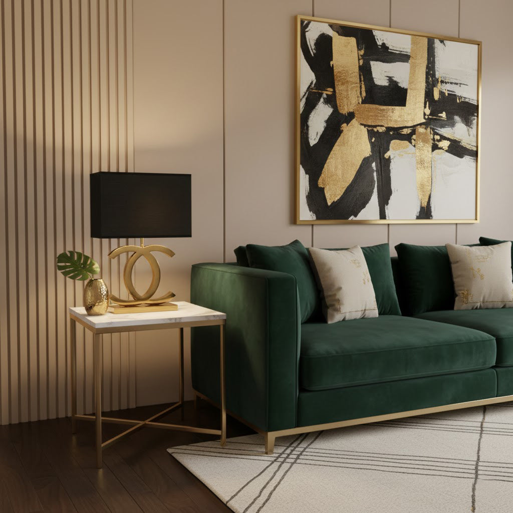 Gold Clérachic table lamp with a black rectangular shade on a marble-topped side table beside a green velvet sofa.