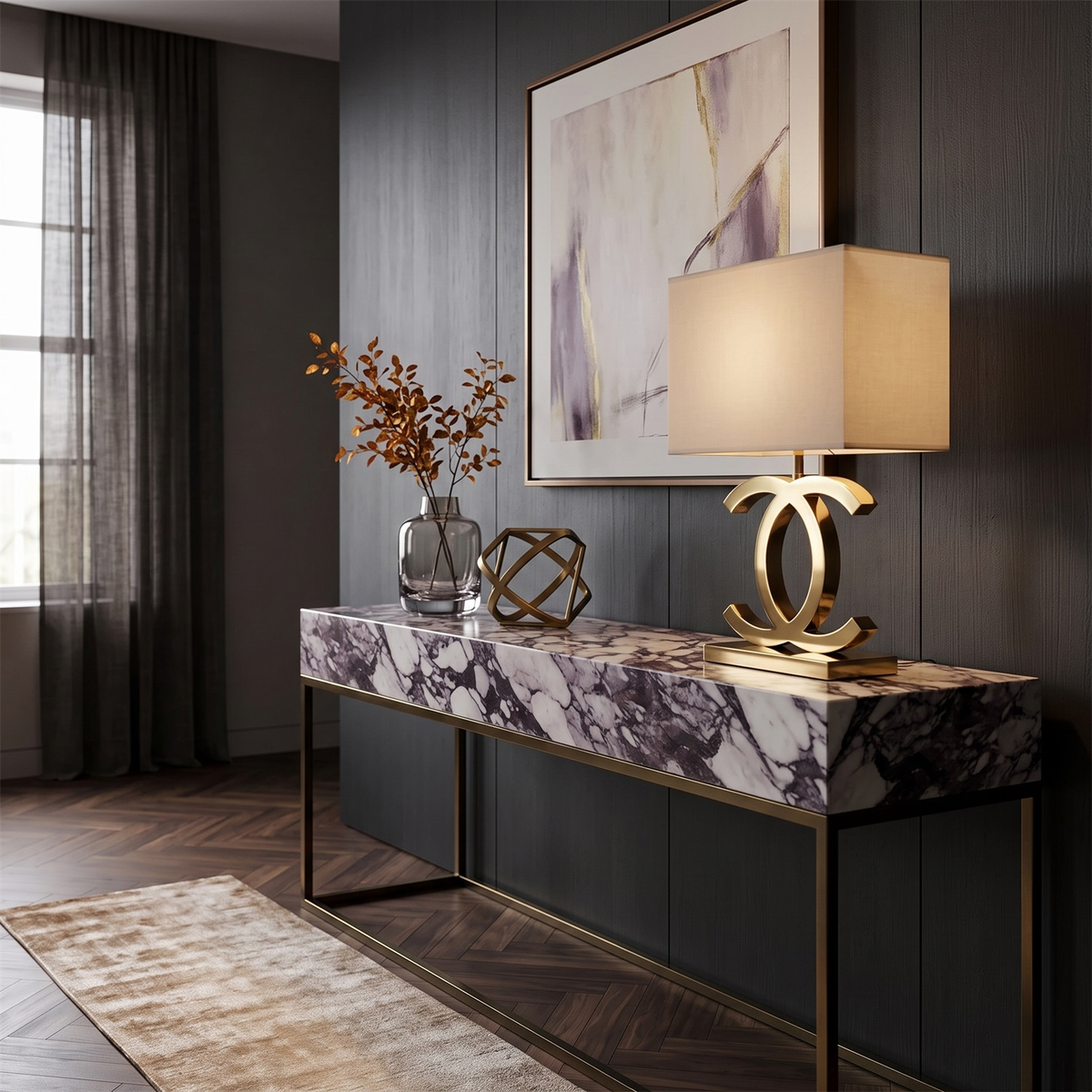 Clérachic gold table lamp with a cream shade on a purple-veined marble console, with a vase of dried stems and a brass sculpture.