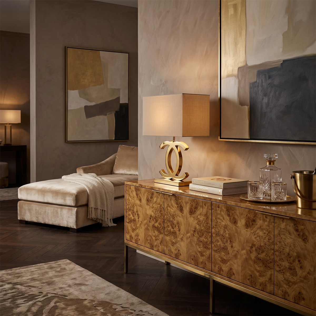 Lit Clérachic gold table lamp with a cream shade on a burr-wood sideboard, beside a decanter and glasses, in a warm, dark-toned room.