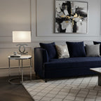 Clérachic table lamp with a white shade and a chrome-toned base on a round side table beside a navy sofa and a black and white print.