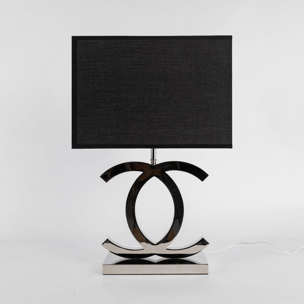 Clérachic chrome table lamp with a black rectangular shade and a polished stainless steel base, against a pale grey backdrop.