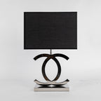 Clérachic chrome table lamp with a black rectangular shade and a polished stainless steel base, against a pale grey backdrop.