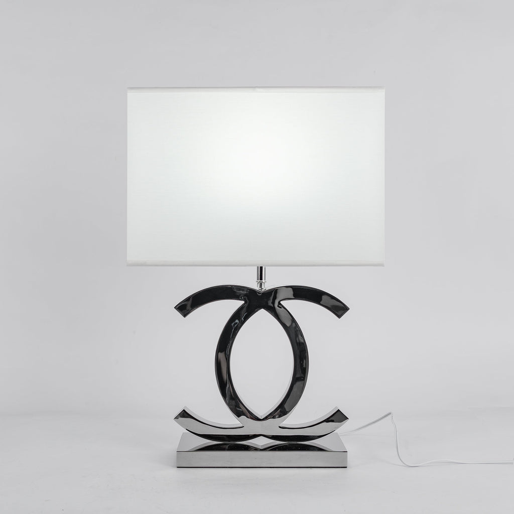 Clérachic chrome table lamp with a white rectangular shade on a polished stainless steel base, against a pale grey backdrop.