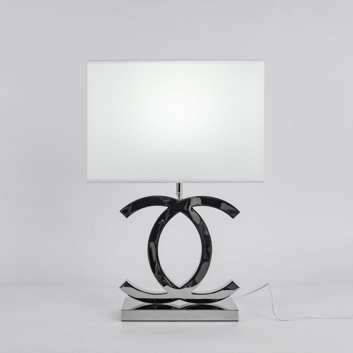 Clérachic chrome table lamp with a white rectangular shade on a polished stainless steel base, against a pale grey backdrop.