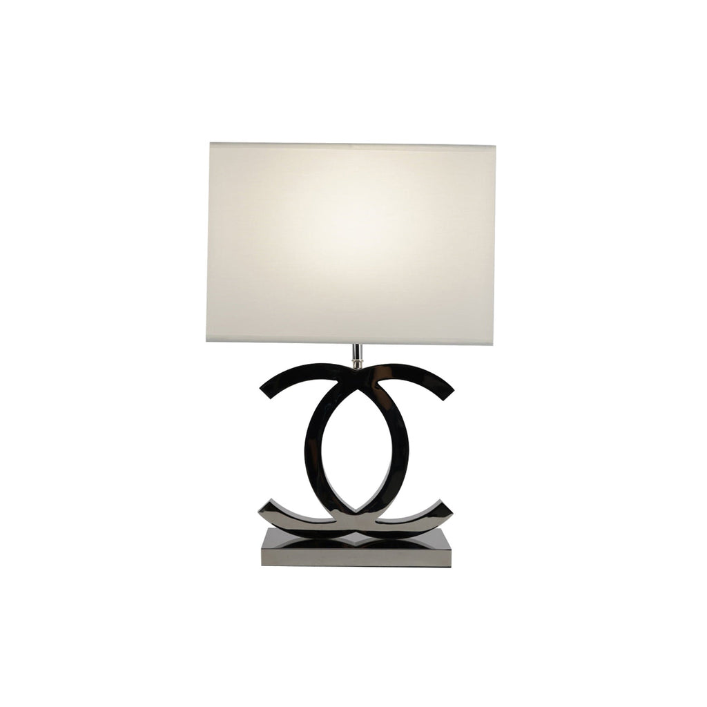 Lit Clérachic table lamp with a white shade and dark chrome loops on a steel base, on a plain white backdrop.