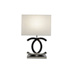 Lit Clérachic table lamp with a white shade and dark chrome loops on a steel base, on a plain white backdrop.