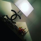 Tilted photo of a Clérachic chrome table lamp with a white shade on a shelf, with small bottles in front and a green wall behind.